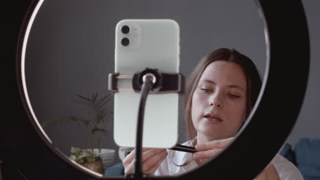 close up of a pretty vlogger female making a video review of a make up brush talking directly to her smartphone's camera