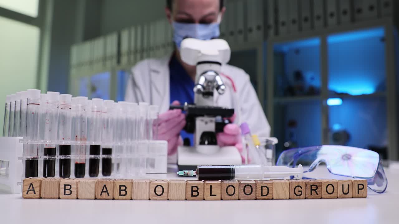 Scientist working in a laboratory with blood samples and a microscope, with 'BLOOD GROUP' spelled out