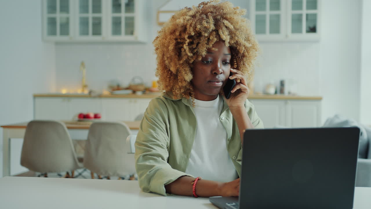 Wanita Muda Afrika-Amerika Berbicara di Telepon dan Bekerja dengan Laptop di Rumah