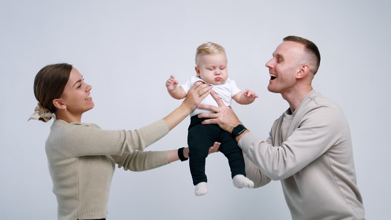 Happy cheerful parents holding their baby from two sides. Mom and dad kiss their beloved child into cheeks.