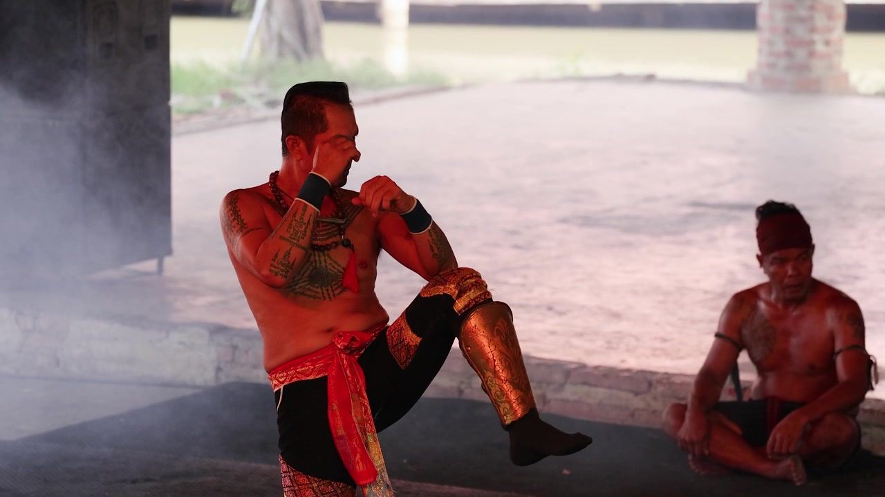 Combattente tatuato esegue movimenti tradizionali di arti marziali in un'arena di allenamento all'aperto e fumosa
