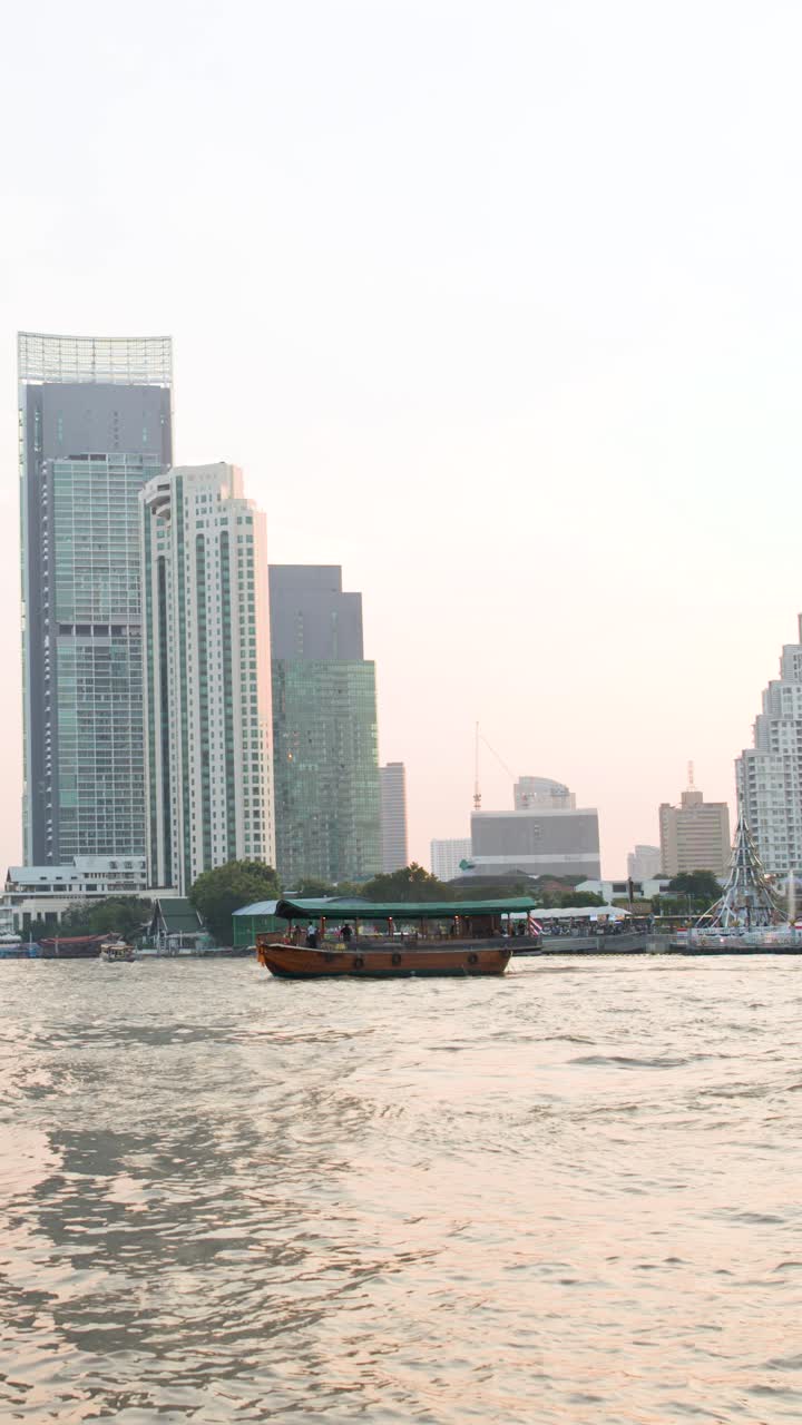 A wooden ferry boat crosses the river against a backdrop of modern city skyscrapers