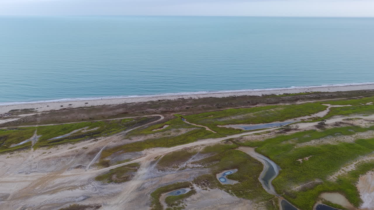 Droneflyfoto fanger de levende grønnfargene og det robuste kystterrenget i La Guajira, Colombia. Rolige havbølger møter de intrikate landskapmønstrene i dette fengslende opptaket.
