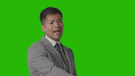 portrait of angry businessman in suit against green screen talking off camera