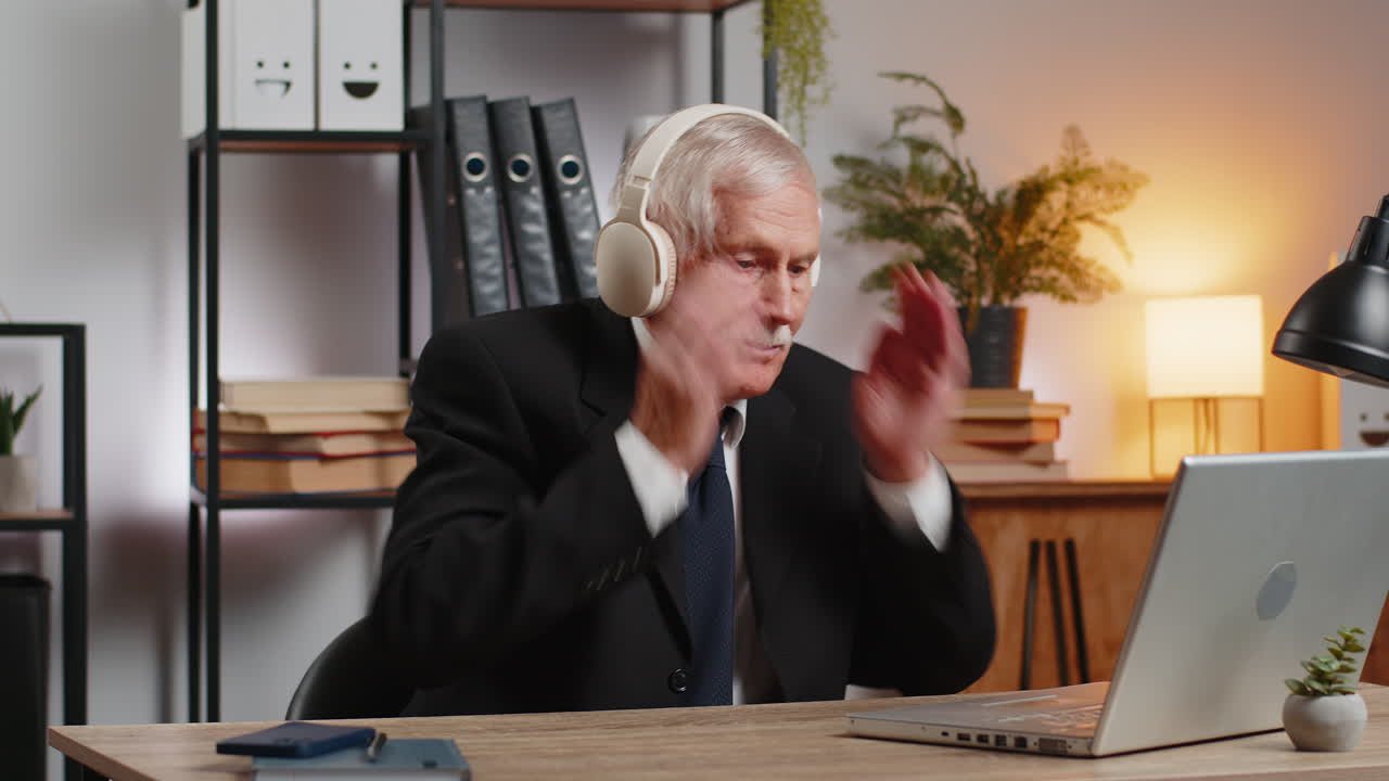 가정 사무실 책상 에서 헤드폰 을 통해 음악 을 듣고 앉아 있는 즐거운 고위 사업가