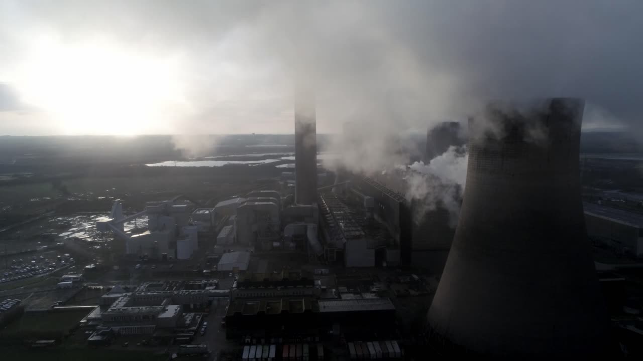 Aerial view of UK power station cooling towers flying through smoke steam emissions at sunrise