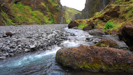 Reveal-of-a-mountain-stream-flowing-on-the-bottom-of-a-beautiful-ravine-with-walls-covered-in-a-green-orange-moss