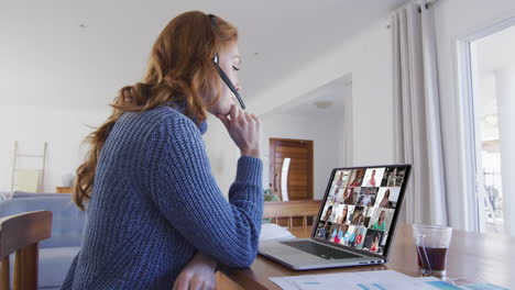 mujer caucásica usando portátil y auriculares de teléfono en videollamada con colegas