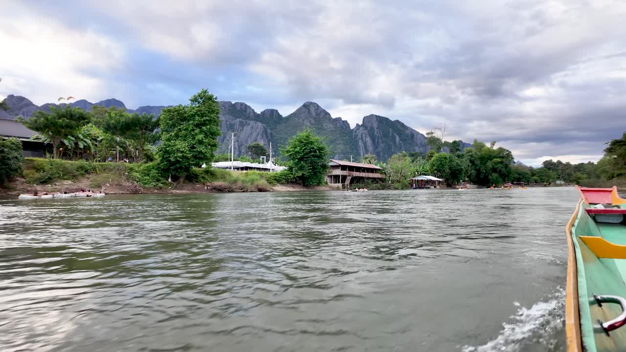 Boat cruising along Nam Song river with karst mountains and lush greenery in Vang Vieng