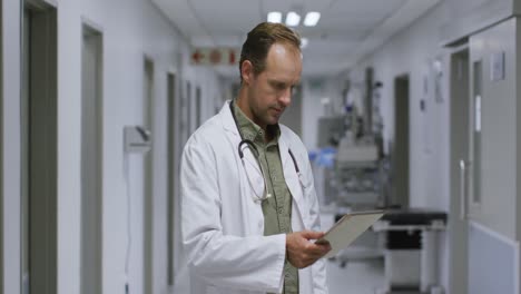 Portrait-of-caucasian-male-doctor-smiling-while-using-digital-tablet-in-the-corridor-at-hospital