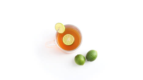 té de limón en una taza de vidrio transparente con limón entero y en rodajas en un plano superior giratorio de fondo blanco