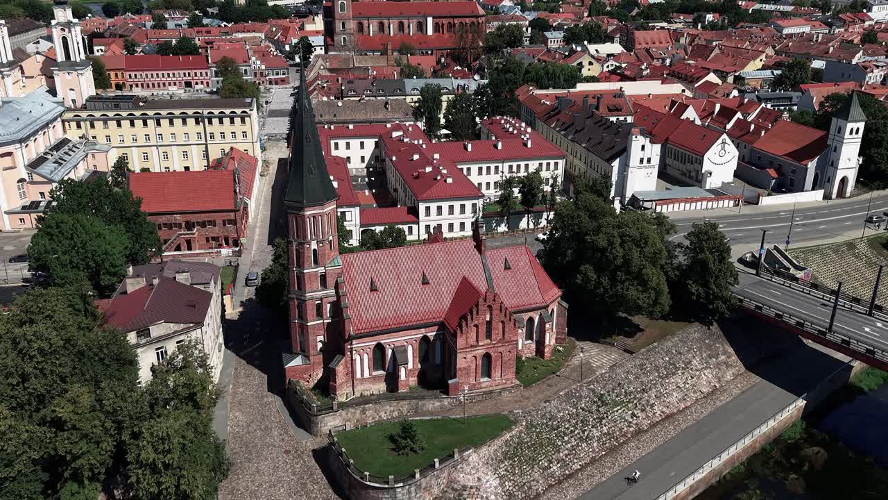 Aerial view of a European city with a historic red-roofed church, river, and surrounding oldtown architecture under a dramatic summer sky