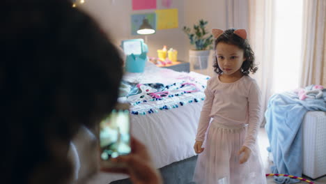 Una-Niña-Feliz-Jugando-A-Disfrazarse-En-El-Dormitorio-Con-Su-Madre-Tomando-Fotos-Usando-Un-Teléfono-Inteligente-Para-Compartir-En-Las-Redes-Sociales