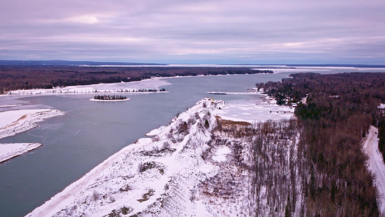Riprese drone che catturano una baia parzialmente ghiacciata del Lago Superiore con un vasto e vuoto paesaggio invernale di fronte.
