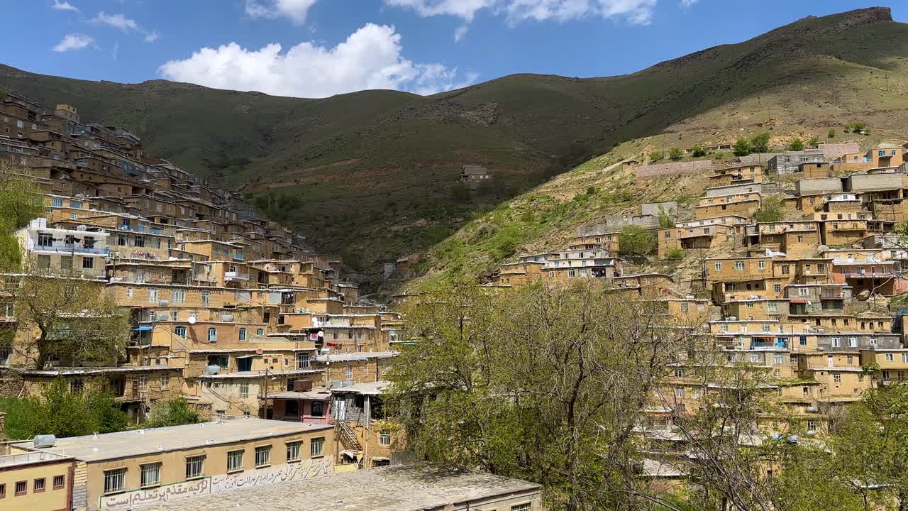 Ombra di nuvole che si alza sulle montagne sotto un cielo blu con nuvole bianche, un villaggio in Iran abitato dal popolo curdo. Natura vivida, pacifica e scenografica del Kurdistan con case a gradoni in mattoni, pendii scoscesi dei monti Zagros, architettura tradizionale in pietra con terrazze e cortili.