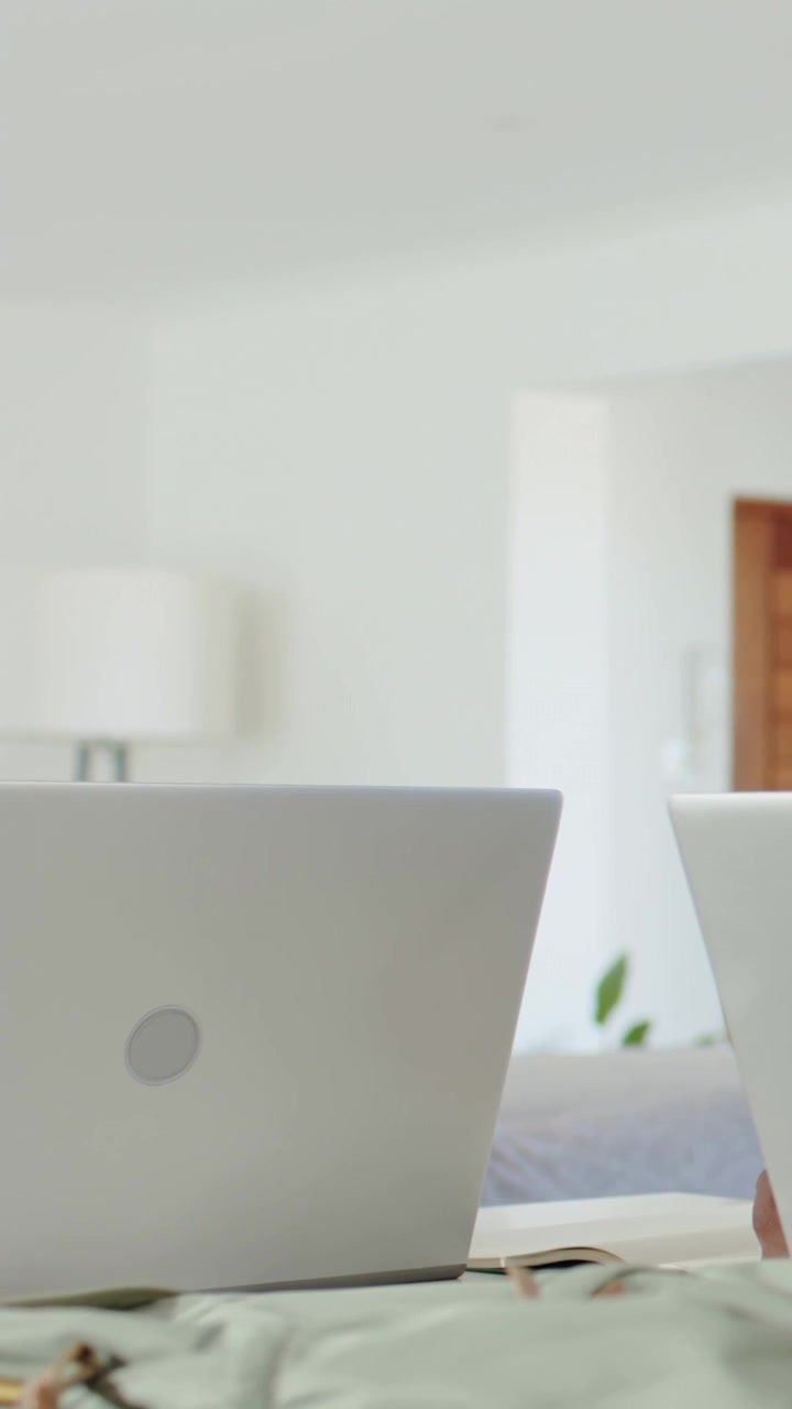 Vertical video: Camera panning silver laptop, woman typing at home, peer taking white cup for work