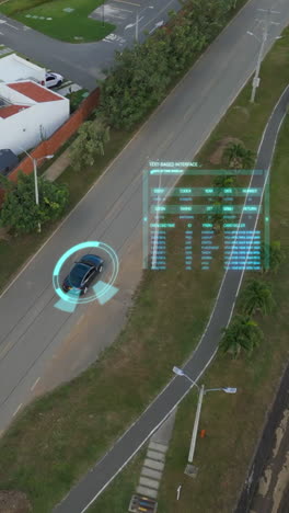Aerial view vertical video of a self-driving car on a quiet suburban road, surrounded by greenery, in bright daylight with holographic data overlay, ideal for mobile content