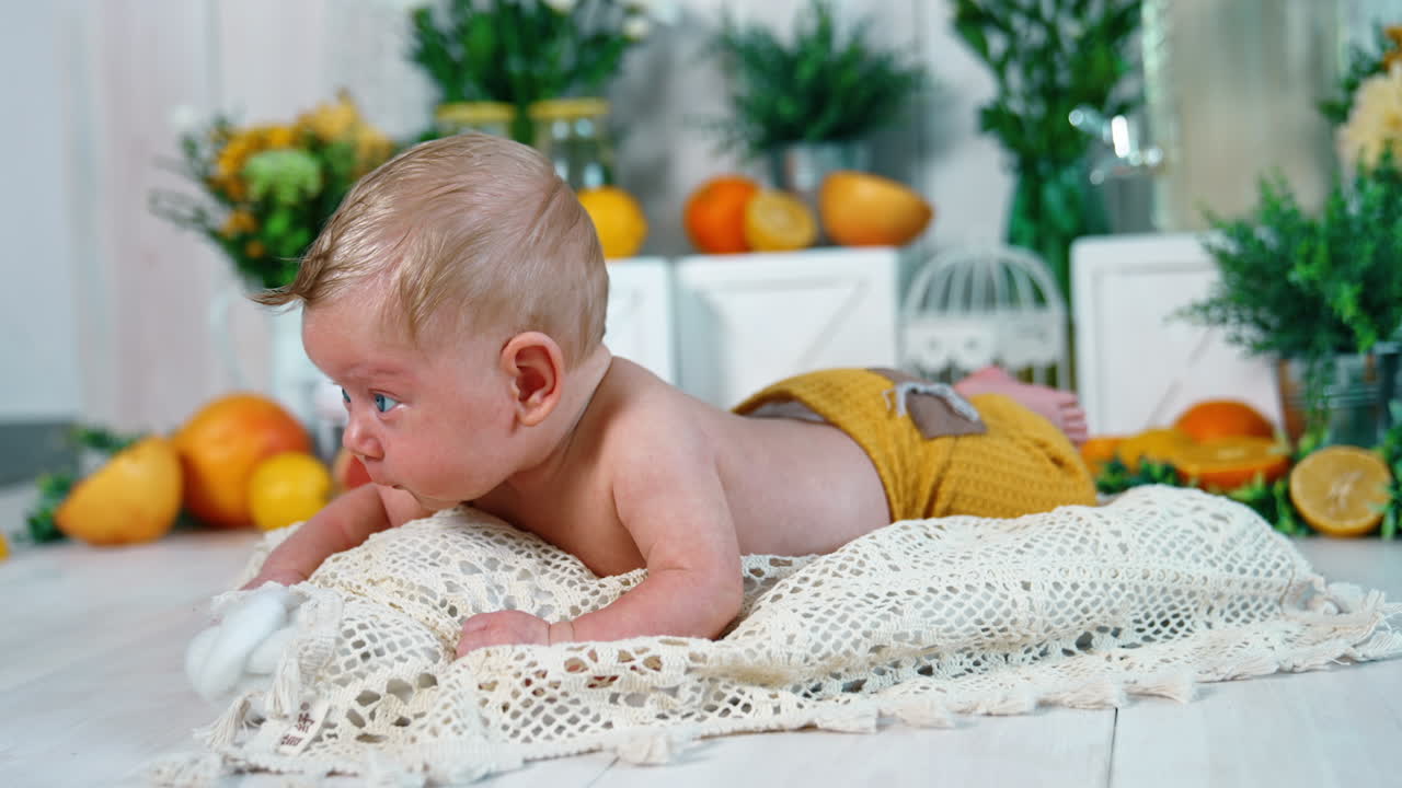 Blond infant boy with amazing blue eyes lies on the knitted plaid. Cute baby lying on belly trying to keep head up.