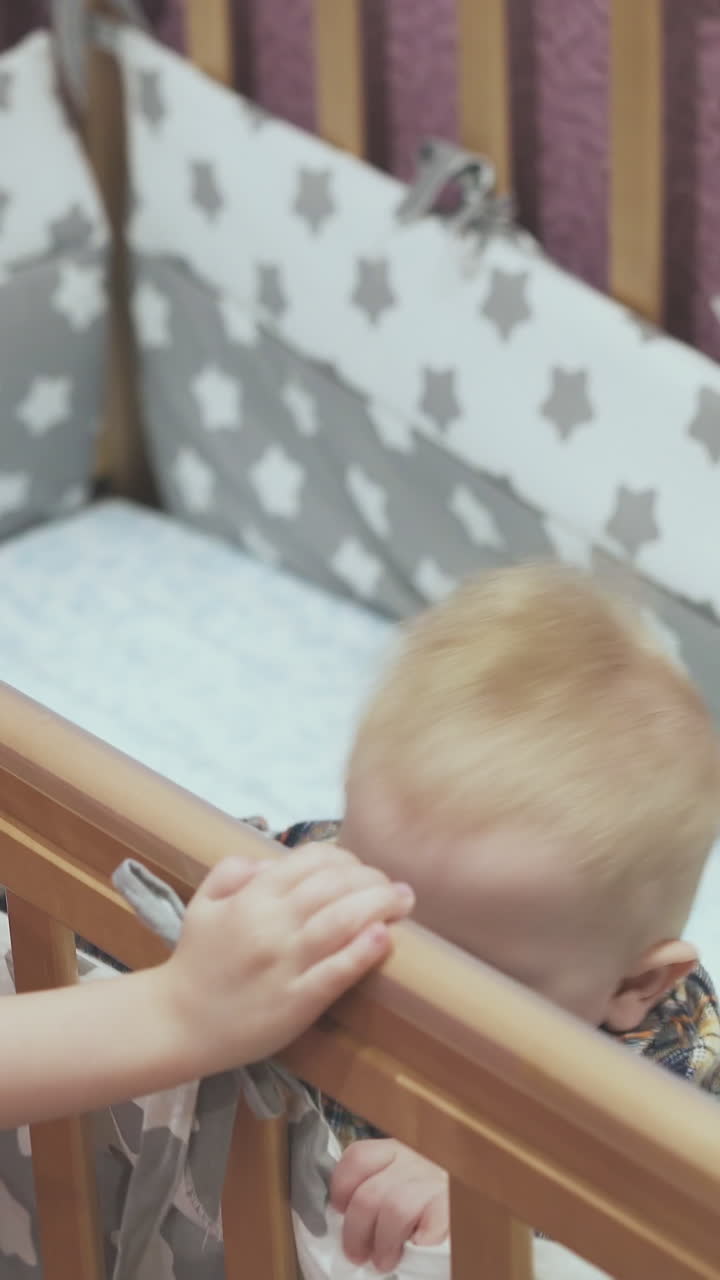 curly haired girl plays with little brother standing in wooden cot in light children room at home closeup