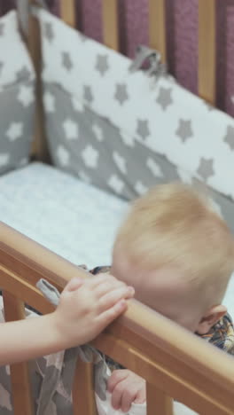 curly haired girl plays with little brother standing in wooden cot in light children room at home closeup
