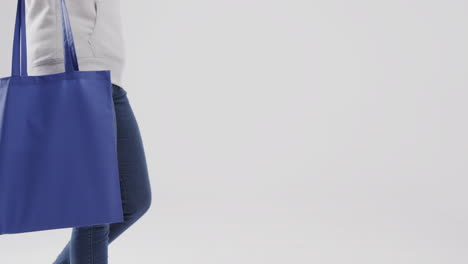 mujer caucásica con capucha blanca sosteniendo una bolsa azul sobre fondo blanco, espacio de copia, cámara lenta