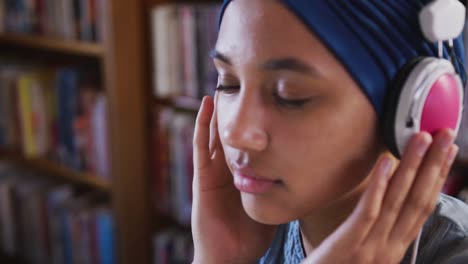 Asian-female-student-wearing-a-blue-hijab-sitting-and-listening-to-music-at-library