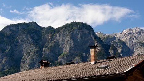 house roof with chimney backdrop by rocky mountains in summer. - timelapse shot