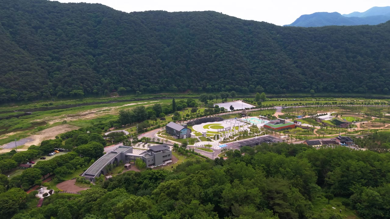 숲이 우거진 장암산 배경 아래 평창 바위 공원 원형극장 정원과 수영장을 보여주는 항공 패럴랙스 샷.