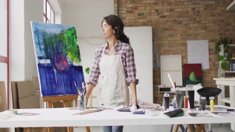 Video-of-biracial-female-artist-standing-at-desk-in-studio