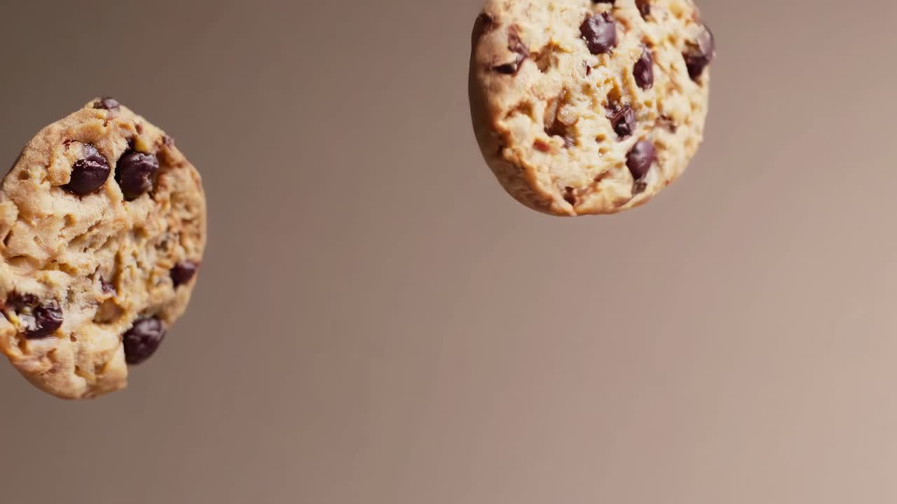 Close-up video of two chocolate chip cookies floating against a neutral background