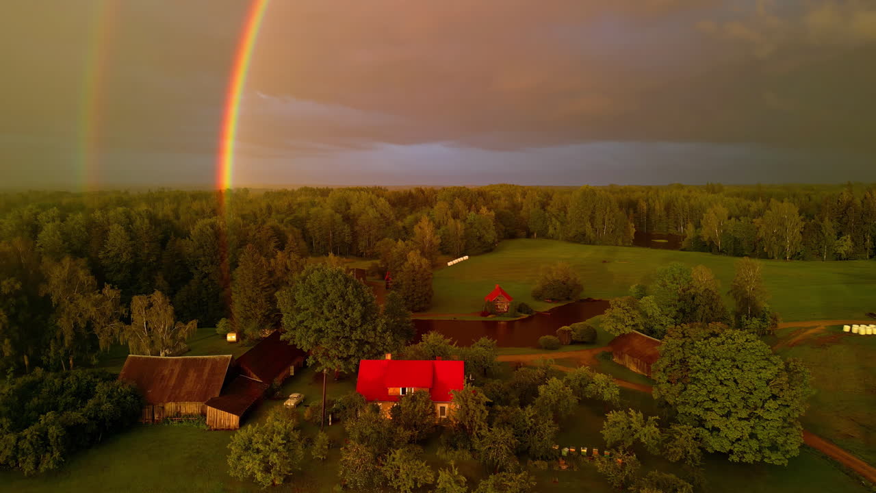 drone aéreo zoom en la toma de arco iris doble sobre las casas de la aldea a lo largo del paisaje verde en un día nublado