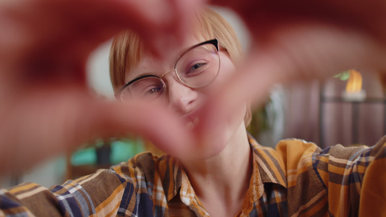 una joven feliz hace un símbolo de amor mostrando un corazón a la cámara para expresar sentimientos románticos