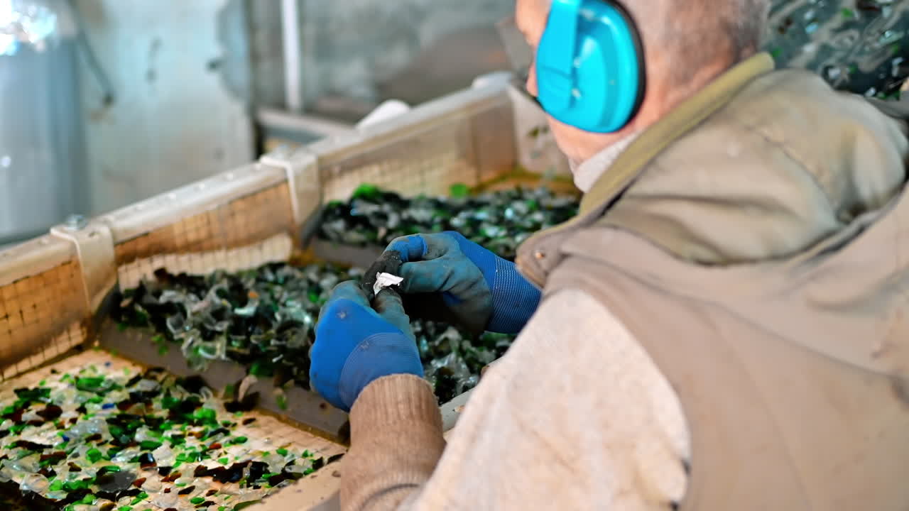 Worker in special gloves sorting glass garbage on a vibrating conveyor belt at waste sorting plant. Slow motion