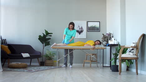 two girls in a beauty salon master in a bathrobe and gloves doing the procedure to remove hair on the legs with a sugar mixture