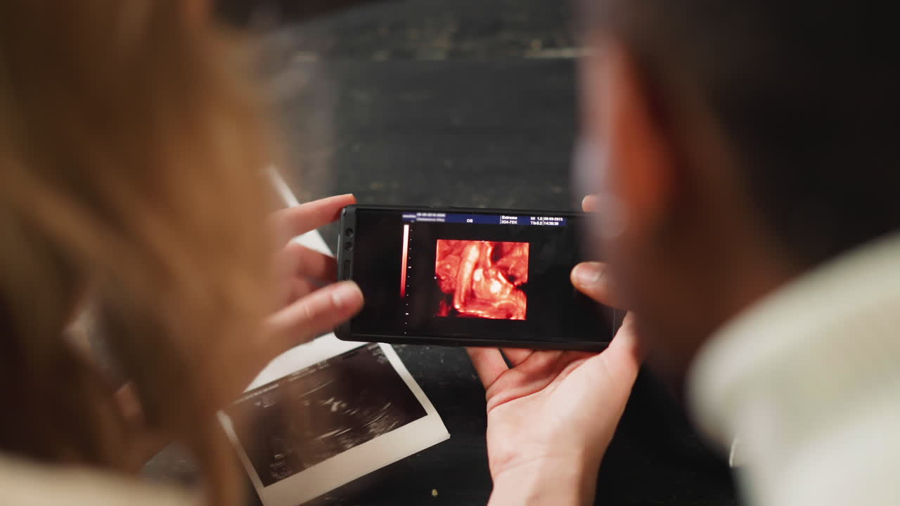 Family watches baby ultrasound record on smartphone screen