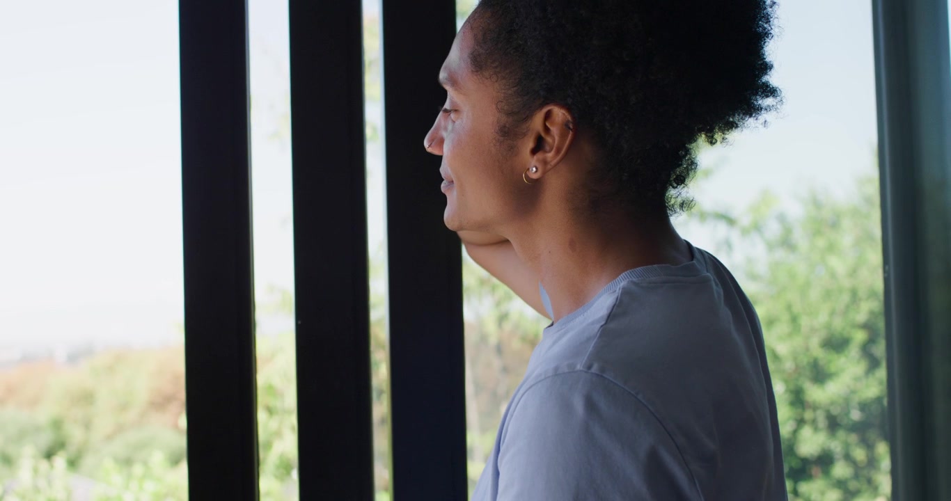 African American man in blue shirt by door shading eyes from sun viewing balcony, copy space