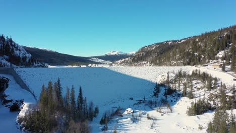 Tunhovd-dam-and-water-magazine---Aerial-approaching-snow-covered-dam-from-far-to-near-with-mountains-and-blue-sky-nature-background---Statkraft-dam-for-Nore-hydroelectric-powerplant-Norway