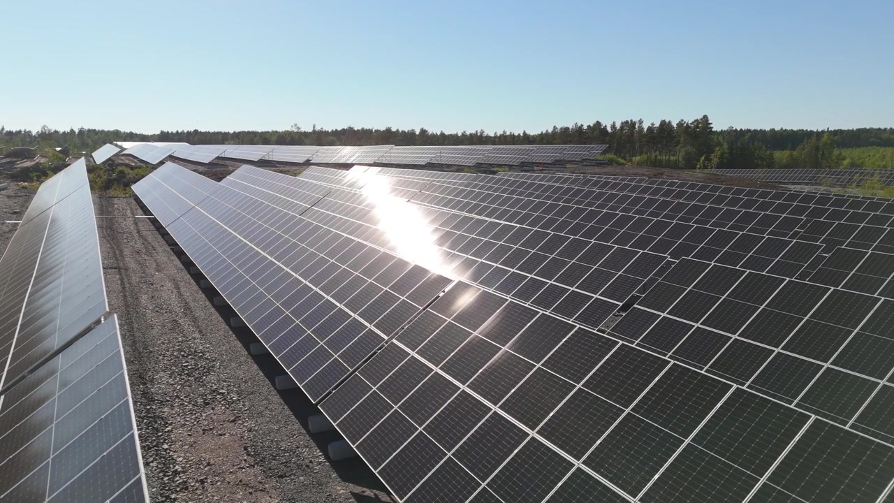 Drone in orbita aerea bassa a destra sopra pannelli solari bifacciali in un parco solare in Finlandia con un raggio di luce che luccica sulla parte superiore.