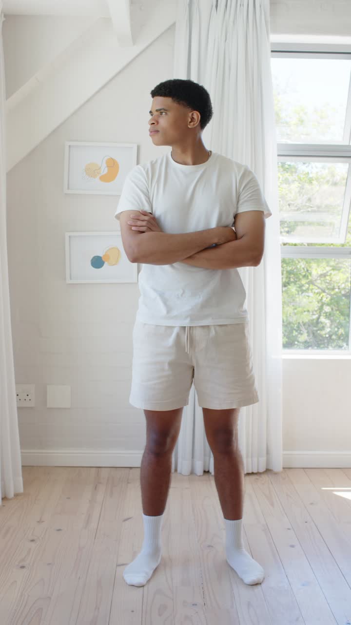 Vertical video: Man standing by window in bright room, noticing camera, shifting gaze, smiling