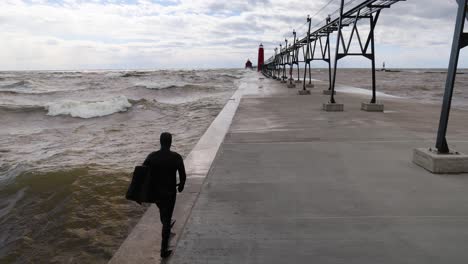 Walking-behind-a-surfer-on-the-Grand-Haven,-Michigan-pier-on-Lake-Michigan