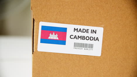hands applying made in cambodia flag label on a shipping cardboard box with products