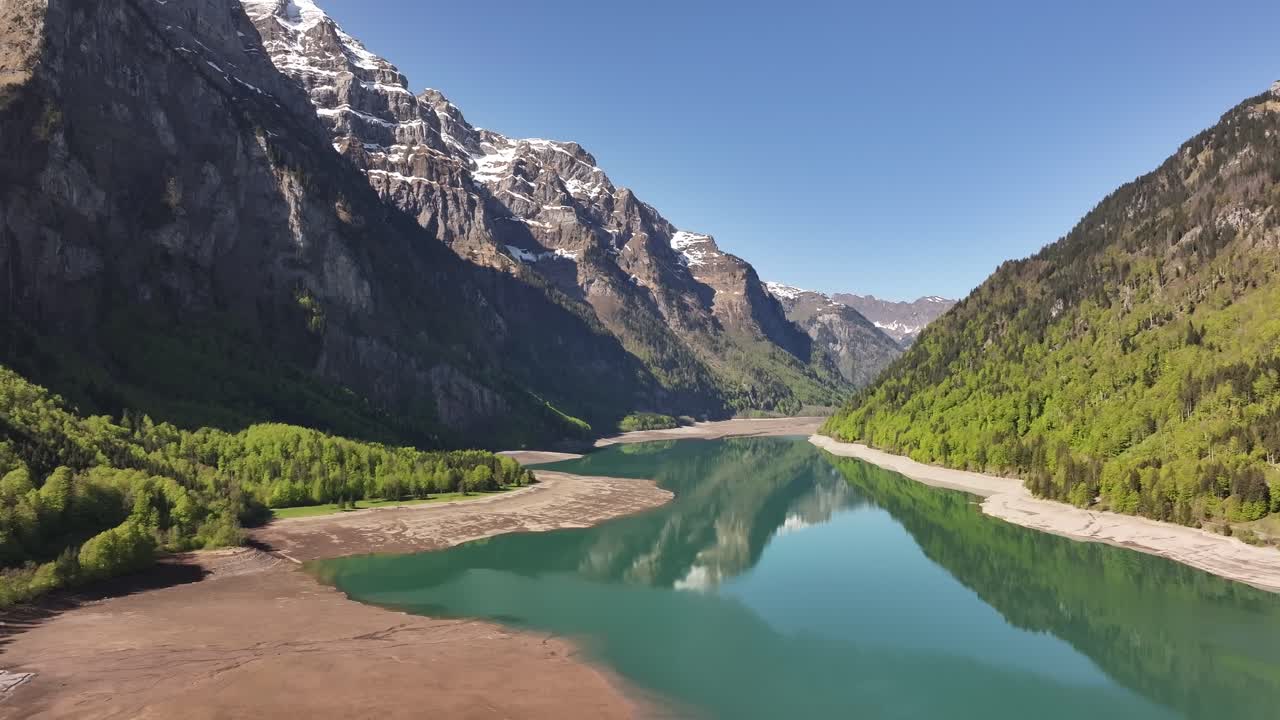 Aerial drone gliding above Klöntalersee in Swiss alps, with still turquoise water and towering mountain reflections
