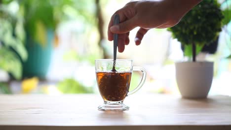 an adult hand is stirring a glass of tea on the table in the morning