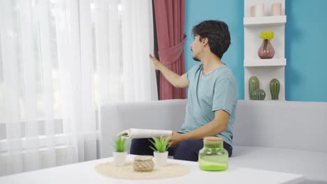 the man opens the closed curtains in his house.