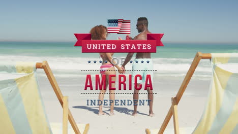 independence day text against african american couple holding hands and toasting drinks at the beach