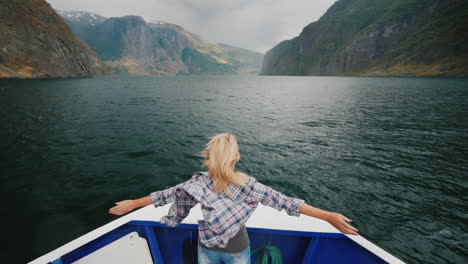 a woman is standing on the bow of the ship sailing over the fjord in norway enjoys the journey the w