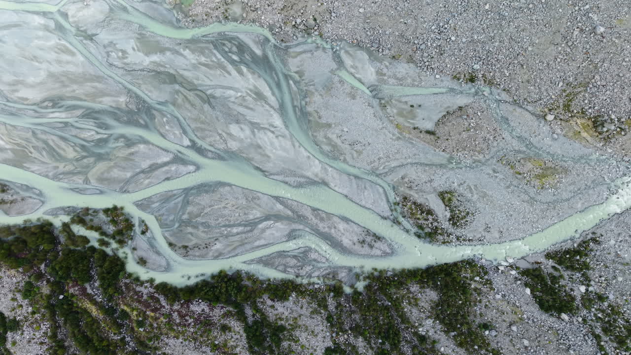 Drone pans sideways above frozen glacial river with rocks and sunlight reflections