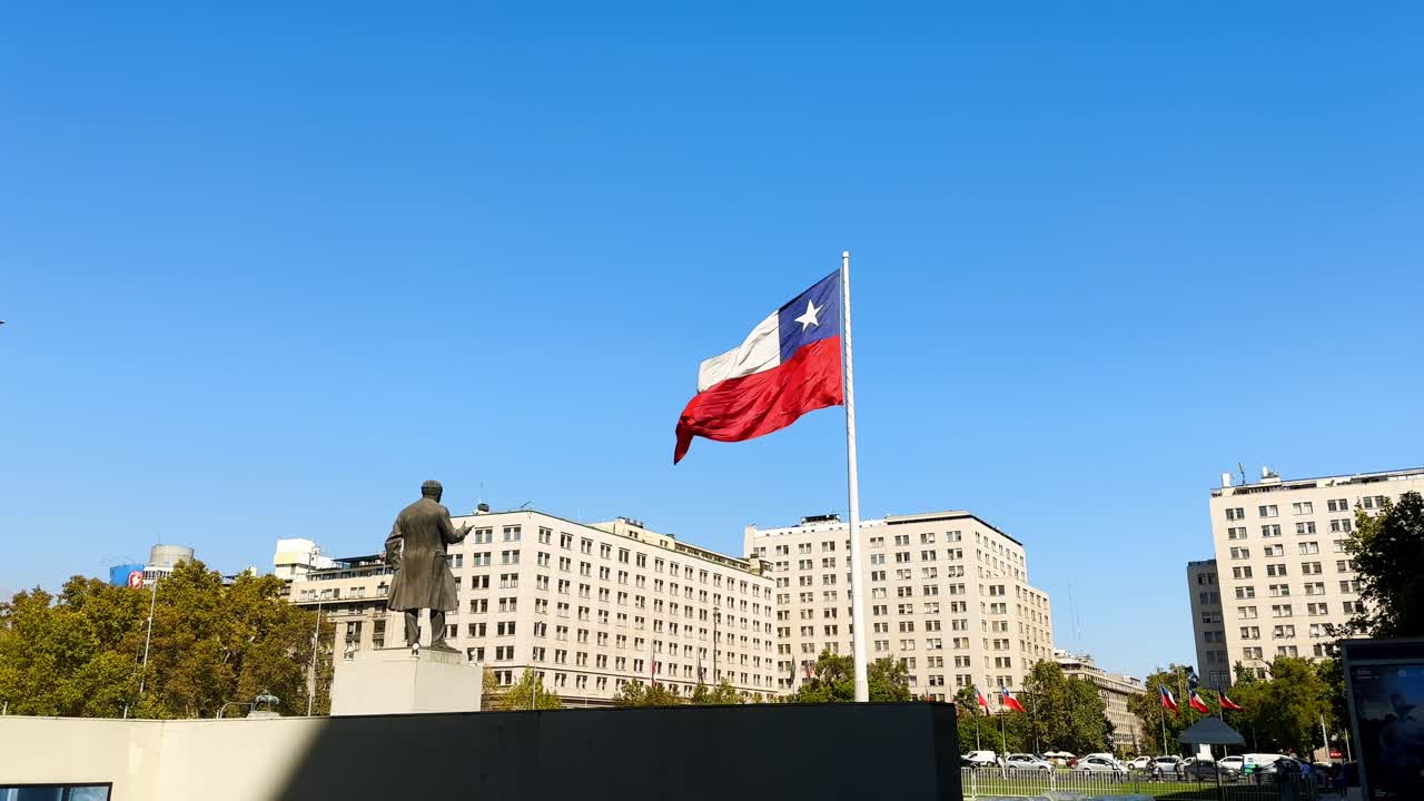 Panoramic slow motion Chile chilean flag waving in the wind above government building, La Moneda architecture, national emblem in urban green park and skyline