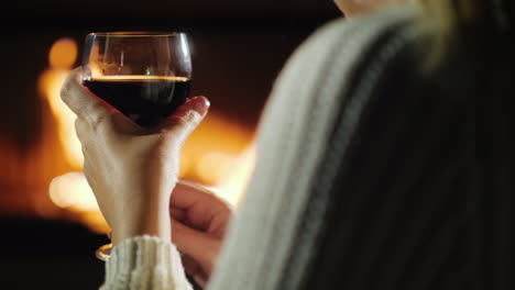 mano con una copa de vino de una mujer que se relaja junto a la chimenea