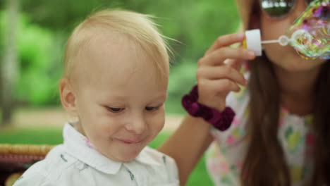 small boy eating cherry at picnic in forest. girl blowing soap bubbles at camera